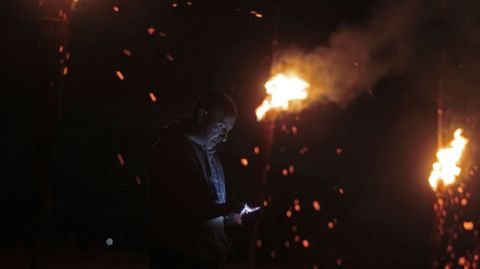 Un hombre consulta su telfono mvil mientras arden las fachas en lo alto del castro de Castelo