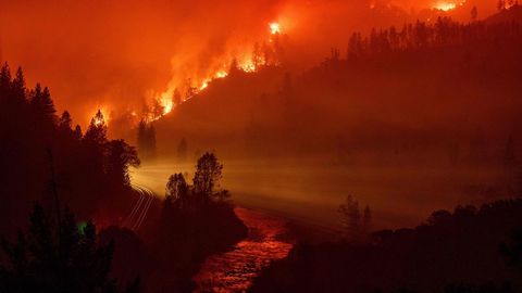 La luz de un tren procedente de una curva se observa en mitad de un valle cercado por las llamas, junto al ro Sacramento, en California