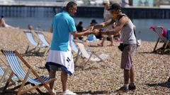 Un hombre cobra el servicio de una tumbona a un baista en la playa de Brighton