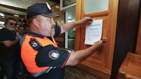Miembros de protección civil de Mugardos colocan un bando municipal en establecimientos hostelereos alertando de la restricción