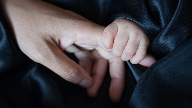 Un beb� coge a su madre de la mano, en una imagen de stock.