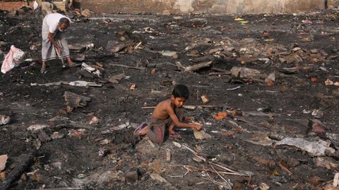 Un nio rohingya busca sus pertenencias entre restos calciandos de un asentamiento temporal en Nueva Dehli