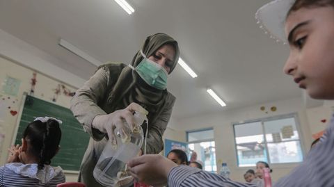 Una profesora desinfectando las manos a una nia palestina dentro de su clase