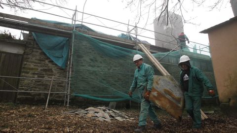 Dos trabajadores retiran una de las losas de pizarra del tejado de la iglesia