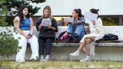 Un grupo de jóvenes repasan en un banco antes de entrar a realizar los exámenes de la ABAU.